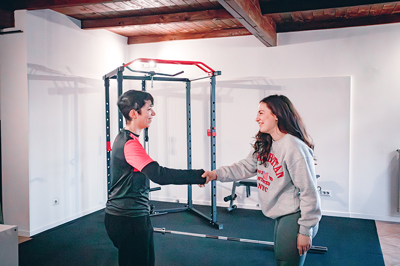 Due donne in tuta si stringono la mano in una palestra.