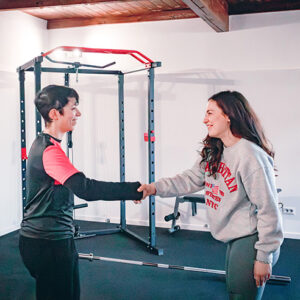 Due donne in tuta si stringono la mano in una palestra.